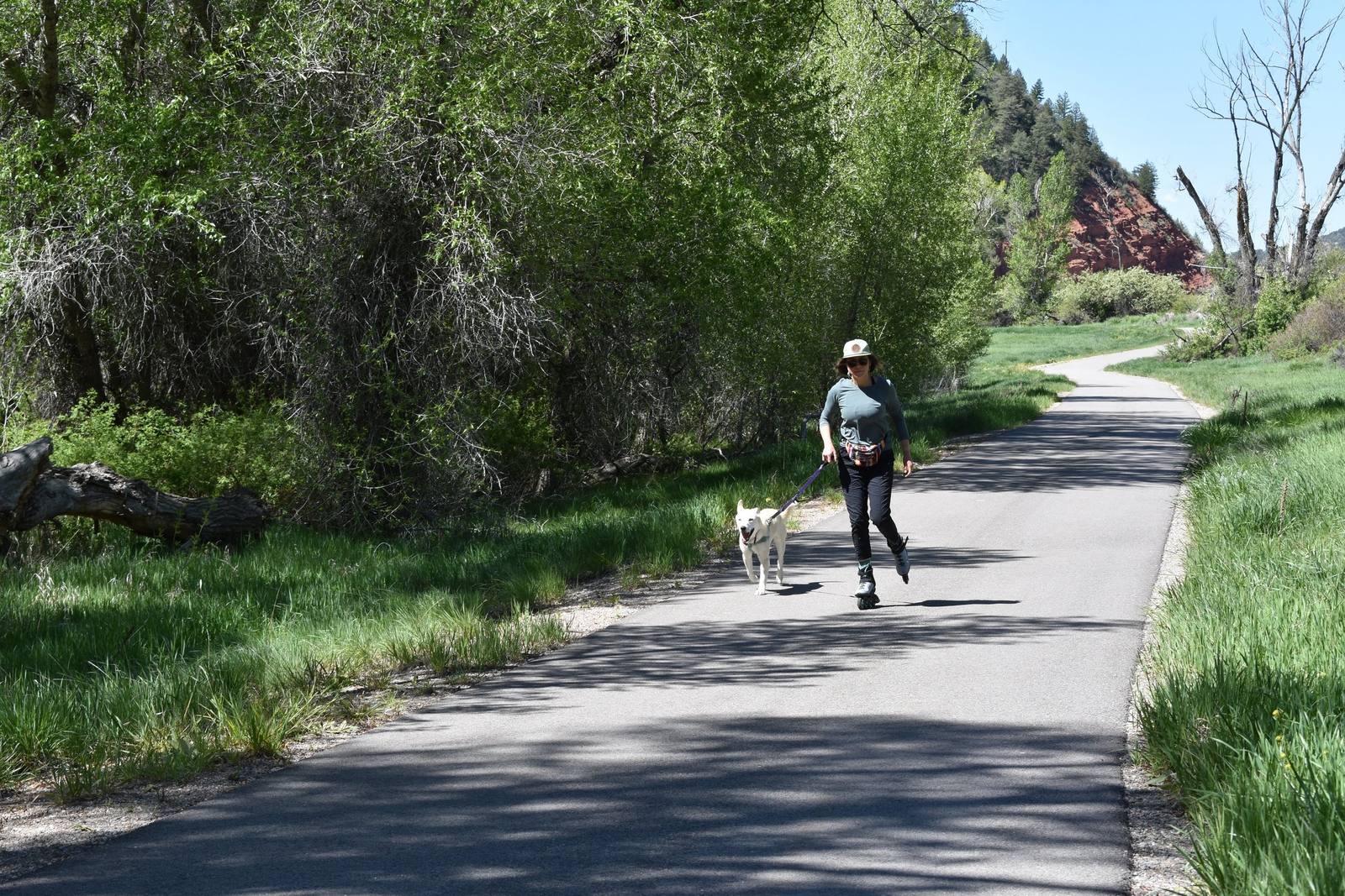 A trail user rollerblades with her dog along the paved Eagle Valley Trail.