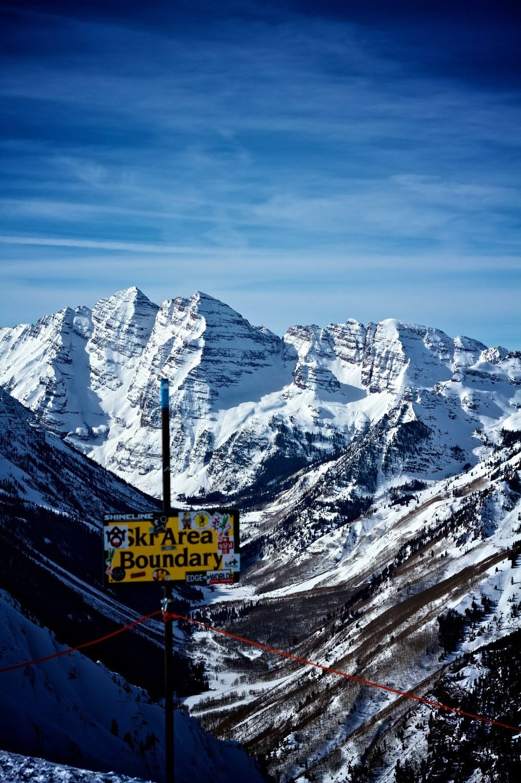 A ski area boundary sign with the Maroon Bells beyond. Crossing the rope means leaving avalanche-controlled terrain.